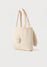 Geantă din blană sintetică de culoare crem, cu două mânere, un pompon pufos pe față și o formă moale, rotunjită pe lateral, pe un fundal simplu.