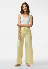 Witte top met vierkante hals en gele gestreepte brede pijpen met een trekkoord in de taille. Model staat met de armen gekruist en draagt platte sandalen.