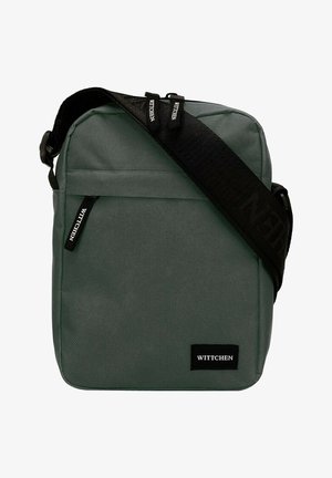Grijze rechthoekige crossbody tas gemaakt van duurzaam materiaal, met een zwarte verstelbare schouderband en logo-applicatie. Voorzak met rits voor extra opbergruimte.