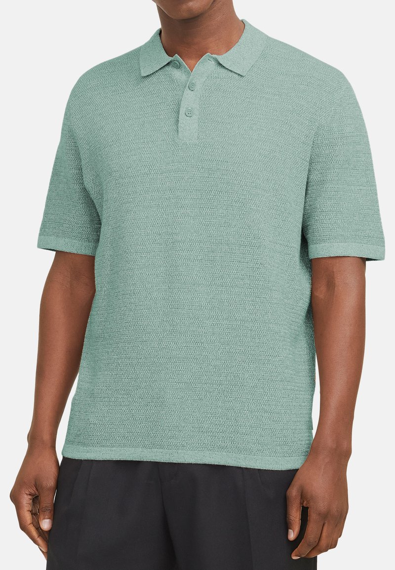 Polo en doux vert menthe, présentant un design en maille texturée, des manches courtes et un col à trois boutons.