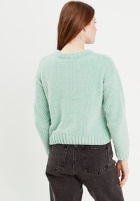 Muntgroene gebreide trui met een gestructureerd patroon, geribbelde kraag en zoom, en een losse pasvorm. Gecombineerd met zwarte hoge taille jeans.