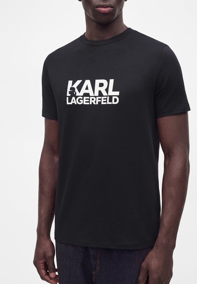 Черна тениска с къс ръкав с бял текст "KARL LAGERFELD" и силуетно лого, носена от човек на изчистен бял фон.