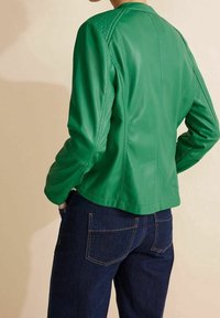Grüne Lederjacke mit taillierter Passform, strukturierten Schulterpanelen und sichtbaren Nähten, kombiniert mit dunklen Jeans. Rückansicht ohne zusätzliche Details.