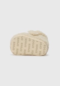 Crème-kleurige fuzzy sloffen met een zachte stoffen bovenkant, rubberen zool met het in reliëf aangebrachte "crocs", en een ronde vorm met een strikaccent.