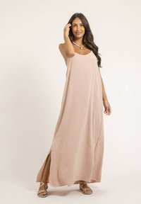 Robe longue sans manches de couleur rose pâle, fabriquée en tissu léger, avec une silhouette fluide et des fentes sur les côtés, assortie à des sandales métalliques.