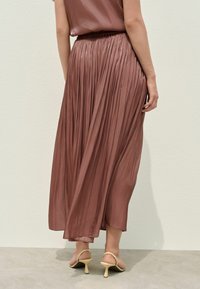 Gonna midi plissettata in un tenue mauve, con una vita arricciata. Il capo ha una texture liscia e scende delicatamente fino all'orlo.