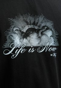 Czarna koszulka z szarym rysunkiem chmur i promieni słońca oraz napisem "Życie jest Teraz" w ozdobnej czcionce.