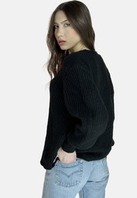 Suéter negro de punto acanalado con mangas largas y un ajuste holgado, combinado con jeans de denim azul claro. La textura es gruesa y densa.