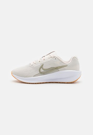Light beige athletic shoes with a mesh upper, green accents, and a white sole. Features a textured surface and orange rubber outsole.