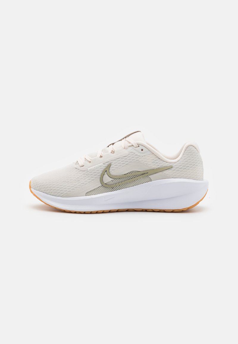 Light beige athletic shoes with a mesh upper, green accents, and a white sole. Features a textured surface and orange rubber outsole.