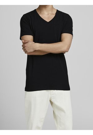 Black v-neck t-shirt with short sleeves and a relaxed fit, made of soft fabric. Paired with light-colored pants. Simple design.