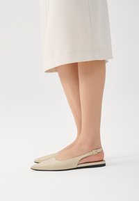Zapatos slingback de cuero beige con punta afilada y una pequeña correa en el tobillo. Suela plana, diseño minimalista y textura suave.