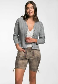 Grauer gerippter Cardigan mit Knöpfen, getragen über einem weißen Spitzentop, kombiniert mit hellbraunen Lederhüften mit floralen Stickereien und seitlichen Bindungen.