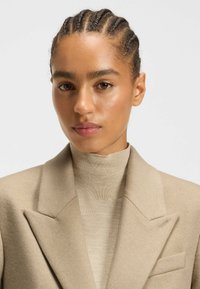 Beige uldeblazer med struktureret krave, der er parret med en matchende finstrikket turtleneck. Glat tekstur, minimal detaljer og skræddersyet pasform.