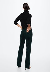 Mustat poolopaidat yhdistettynä tummanvihreisiin samettikankaisiin leveälahkeisiin housuihin, jotka esittelevät sileää tekstuuria ja yksinkertaisia ompeluyksityiskohtia.