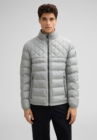 Giacca trapuntata leggera grigia con colletto alto, chiusura con zip frontale e tasche laterali. Presenta polsini elastici e una texture liscia e lucida.
