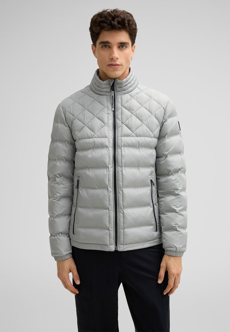 Giacca trapuntata leggera grigia con colletto alto, chiusura con zip frontale e tasche laterali. Presenta polsini elastici e una texture liscia e lucida.