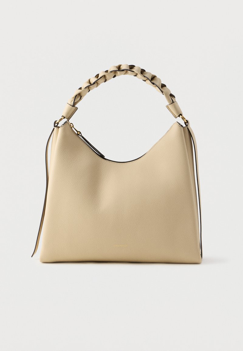 Smėlio spalvos odinė rankinė su pynu rankena ir laisvos formos siluetu. Minimalistinės detales ir kontrastinga kraštų apdaila.