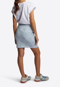 Bílý krátký rukávový top v kombinaci se světle modrou sukni se subtilním pavučinovým vzorem. Model má na sobě šedé a modré tenisky.