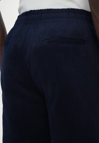 Shorts en velours côtelé bleu marine avec un tissu texturé, une taille élastique et deux poches arrière avec un détail de couture horizontal.