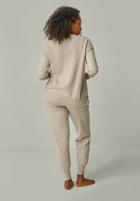 Beige Strick-Loungewear-Set mit einem locker sitzenden Pullover mit gerippten Bündchen und passenden tapered Pants mit Knöcheldetails. Texturierter Stoff.
