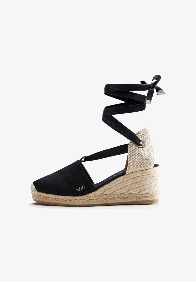 Espadrille wedge in tela nera con suola in juta intrecciata, dotata di cinturini neri incrociati e accentuazione del tallone in beige texturizzato.