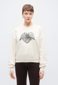 Κρεμ φούτερ με μακριά μανίκια, με μεταλλική καρδιά με τύπωμα λεοπάρδαλης και έντονο κείμενο «AMOUR». Μαλακό, υφασμάτινο με υφή.