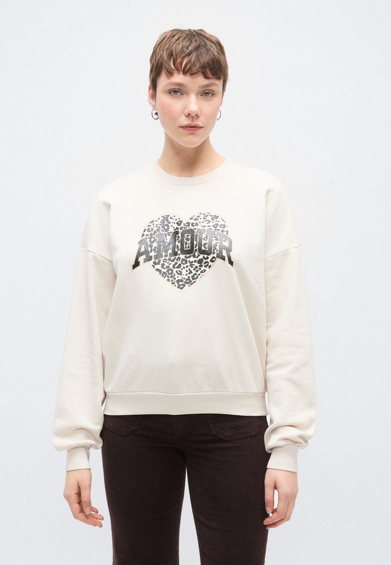 Κρεμ φούτερ με μακριά μανίκια, με μεταλλική καρδιά με τύπωμα λεοπάρδαλης και έντονο κείμενο «AMOUR». Μαλακό, υφασμάτινο με υφή.