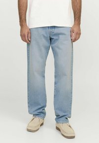 Jeans de denim azul claro con corte recto, con un acabado desgastado y diseño de cinco bolsillos, usados con zapatos beige tipo mocasín.