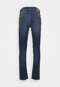 Tummansinisiä farkkuja slim fit -mallilla, joissa on kaksi takataskua ruskeilla ompeleilla, nahkapaikka vyötäröllä ja suora leikkaus.