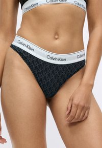 Sorte Calvin Klein thong undertøy med en hvit merket midjebånd, som har et geometrisk mønster på stoffet. Glatt tekstur og tett design.