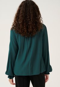 Teal blouse with long, gathered sleeves, featuring a smooth texture and a relaxed fit. The back has a subtle pleat detail.