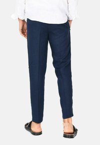 Pantaloni in lino blu navy dalla vestibilità slim, dotati di tasche laterali e una texture liscia, abbinati a sandali neri.