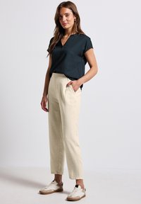 Dark green short-sleeve blouse with a v-neck, paired with light beige tailored trousers, and white sneakers with brown accents.