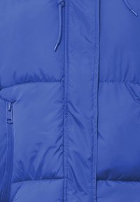 Blå puffjakke med en glat, skinnende tekstur, quiltet design og en frontlynlås. Inkluderer snorejusteringer ved kraven.