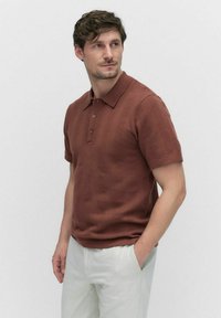 Brun textureret polo-shirt med krave og tre knapstoppede, parret med lyse bukser.