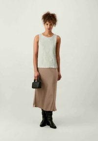 Helehall tekstureeritud ilma varrukateta topp, mis on ühendatud beeži midi seeliku ja kuni põlve mustade saapadega, hoides väikest musta käekotti.