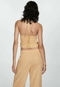 Hellgelbes, ärmelloses Cropped Top mit Rückengeknoteten und strukturiertem Stoff, kombiniert mit passenden hoch taillierten Hosen mit Cargo-Taschen.
