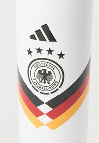 Το λογότυπο της Adidas πάνω από τέσσερις αστέρες και ένα έμβλημα της Γερμανικής Ποδοσφαιρικής Ομοσπονδίας με μαύρες, κόκκινες και χρυσές διαγώνιες λωρίδες σε λευκό φόντο.