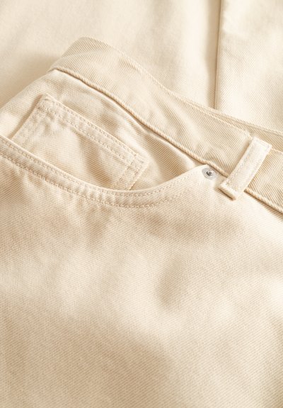 Béžové bavlnené nohavice s hladkou textúrou, s vreckom na zadnej strane, prešívanými detailmi a kovovým gombíkom ako doplnkom.