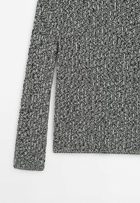 Langärmliger Sweater in Schwarz-Weiß-Melange mit geripptem Textur, von der Schulter bis zur Taille auf einem weißen Hintergrund gezeigt.