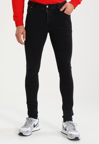 Černé skinny džíny vyrobené z denimu, s klasickým pětipocket designem a zapínáním na knoflík. Nosit s šedými teniskami a červeným topem.