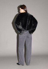 Schwarze Kunstfelljacke mit einem kurzen, oversized Design; kombiniert mit hochgeschnittenen grauen Jeans; glatte Textur und lässige Silhouette.