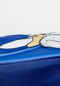 Sac en tissu bleu avec une surface texturée, présentant un graphisme de personnage en blanc, beige et vert. Le design met l'accent sur la couleur et le détail.