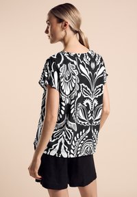 Top a fiori in bianco e nero con maniche corte e vestibilità rilassata, realizzato in tessuto leggero, abbinato a pantaloni corti neri.
