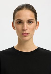 Zwart katoenen T-shirt met een ronde halslijn. De stof heeft een gladde textuur. Kenmerkt zich door een minimalistisch ontwerp zonder zichtbare patronen of accenten.