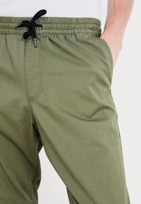 Gröna byxor med elastisk midja och svart snörning, med sidofickor och en jämn, lätt tygtextur.