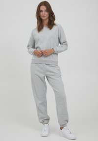 Ensemble composé d'un sweat-shirt et d'un pantalon de jogging gris en tissu doux, avec des poignets et une taille côtelés. Assorti à des baskets blanches.