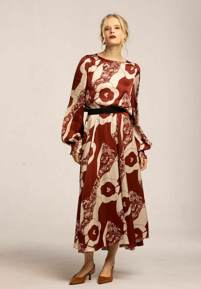 Lång, flödande klänning med ett röd och krämfärgat blommönster, med ett åtsittande svart midjeband och puffärmar. Slät tygtextur.