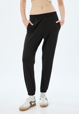 Zwarte joggingbroek gemaakt van zachte stof, met een elastische tailleband, zijzakken en elastische boorden bij de enkels.